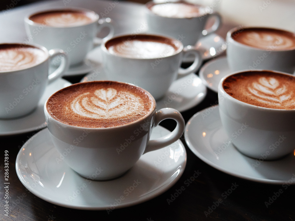 Set of freshly brewed cappuccino cups with milk foam latte art served on bartend table in cozy city cafe lit with natural window light Set of freshly brewed cappuccino cups with milk foam latte art served on bartend table in cozy city cafe lit with natural window light