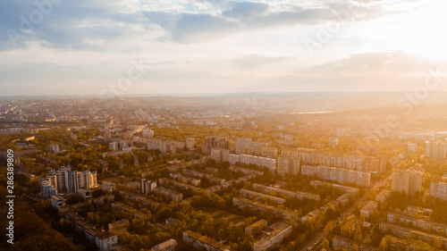 Shot of a city located at the edge of a forest, and a cloudy sky, during sunrise. © Ion