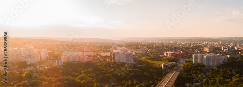 Shot of a highway road located in the middle of a green forest leading towards a big city, during sunrise.