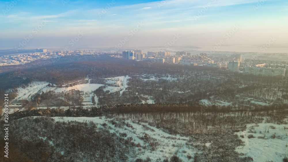 Aerial view of a beautiful city and a small forest, during a cold, snowy winter.