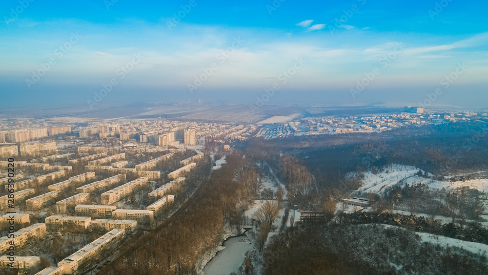 Aerial view of a beautiful city and a small forest and a frozen lake, during a cold winter.