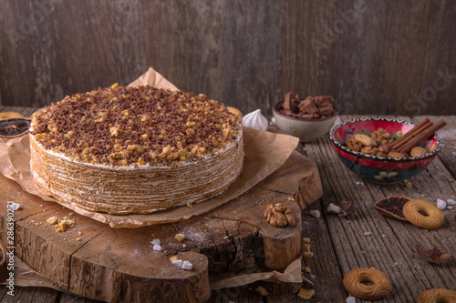 Delicious honey cake with sweet sour cream, chocolate and nuts on a rustic background. View from above. Free space for text.
