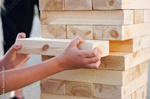 A child takes out one bar from the tower while playing a giant jenga. Outside photo