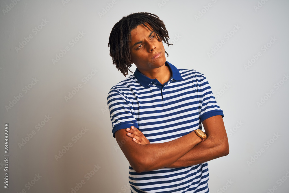 Afro man with dreadlocks wearing striped blue polo standing over isolated white background looking to the side with arms crossed convinced and confident Afro man with dreadlocks wearing striped blue polo standing over isolated white background looking to the side with arms crossed convinced and confident