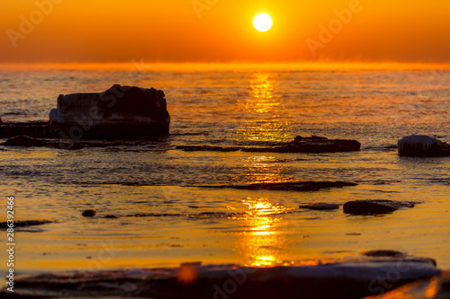 Beautiful seascape. The orange sun rises over the horizon in a blazing sea.