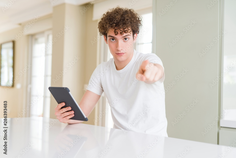 Young man using touchpad tablet pointing with finger to the camera and to you, hand sign, positive and confident gesture from the front Young man using touchpad tablet pointing with finger to the camera and to you, hand sign, positive and confident gesture from the front