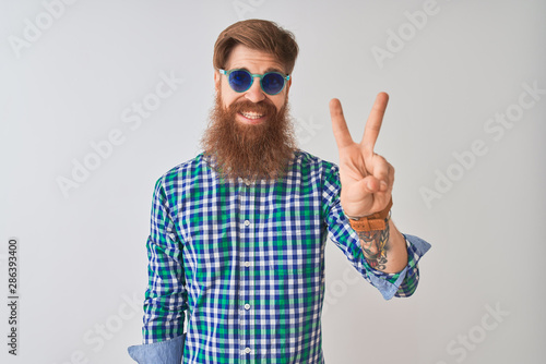 Young redhead irish man wearing casual shirt and sunglasses over isolated white background showing and pointing up with fingers number two while smiling confident and happy.