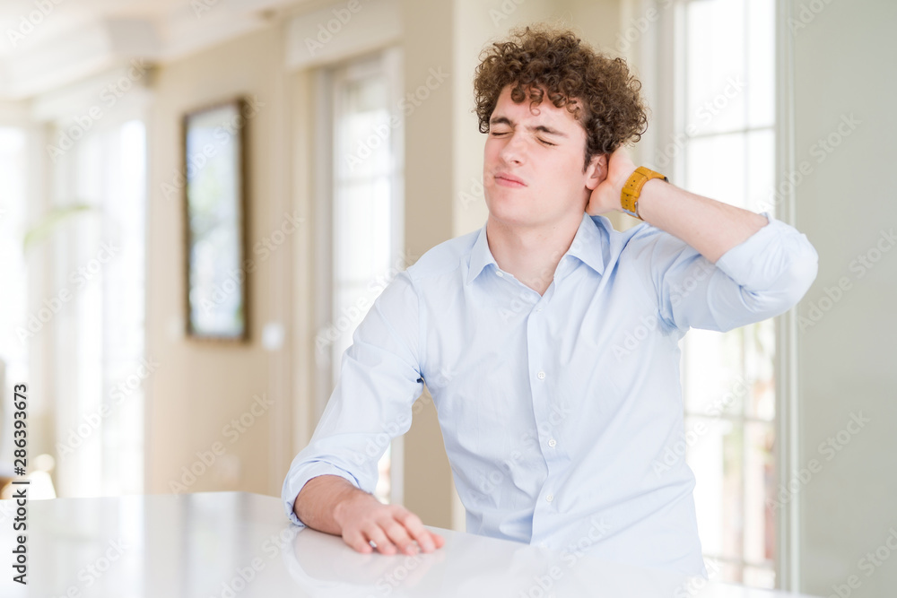 Young business man with curly read head Suffering of neck ache injury, touching neck with hand, muscular pain