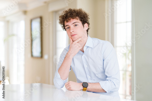 Young business man with curly read head looking confident at the camera smiling with crossed arms and hand raised on chin. Thinking positive.