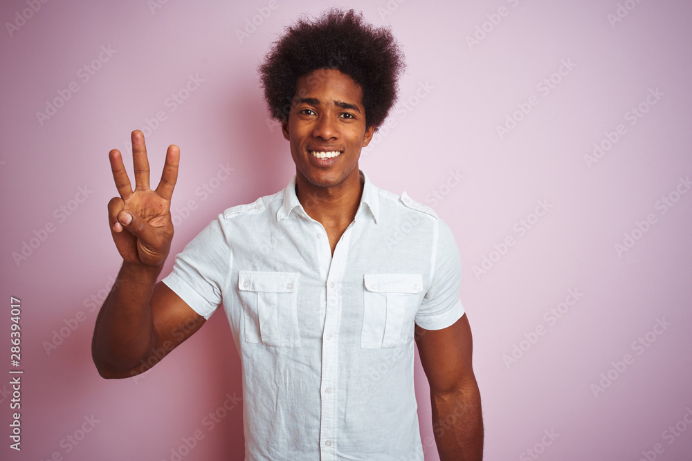 Young american man with afro hair wearing white shirt standing over isolated pink background showing and pointing up with fingers number three while smiling confident and happy. Young american man with afro hair wearing white shirt standing over isolated pink background showing and pointing up with fingers number three while smiling confident and happy.