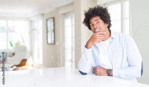 African American man at home looking confident at the camera with smile with crossed arms and hand raised on chin. Thinking positive.