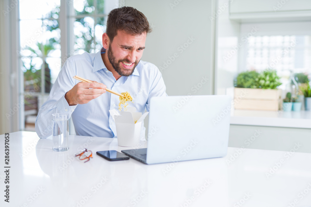 Business man eating take away asian noodles food while working using computer laptop and smiling
