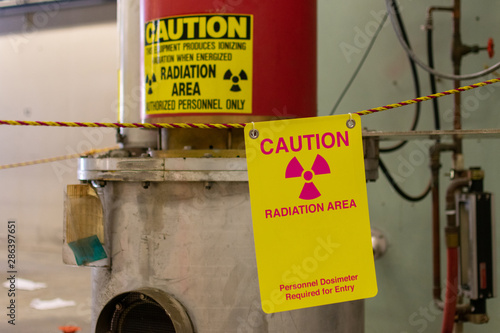 Ionizing radiation hazard symbol, caution radiation area and personnel dosimeter required text on yellow warning sign displayed on the equipment that produces ionizing radiation  photo