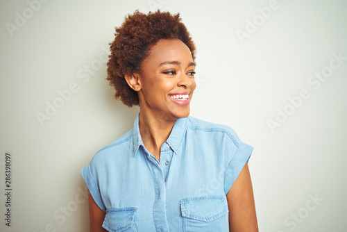Young beautiful african american woman with afro hair over isolated background looking away to side with smile on face, natural expression. Laughing confident.
