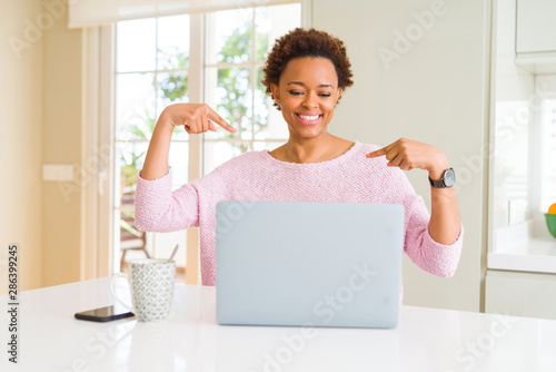 Young african american woman working using computer laptop looking confident with smile on face, pointing oneself with fingers proud and happy.