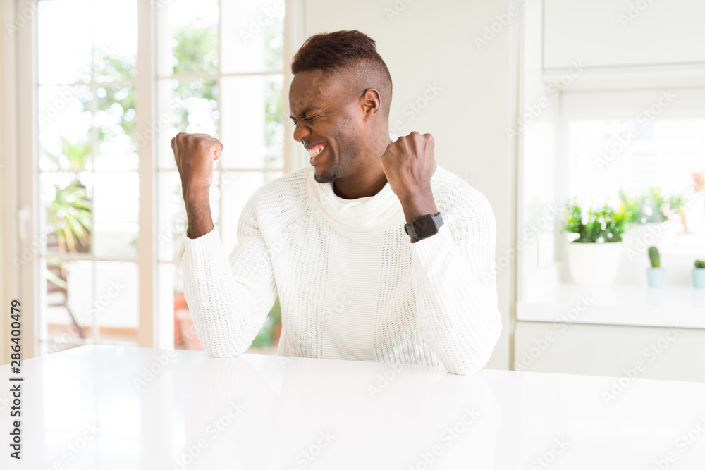 Handsome african american man on white table very happy and excited doing winner gesture with arms raised, smiling and screaming for success. Celebration concept.
