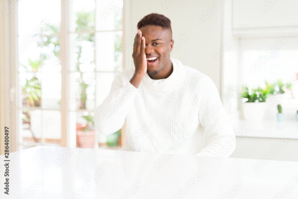 Handsome african american man on white table covering one eye with hand with confident smile on face and surprise emotion.