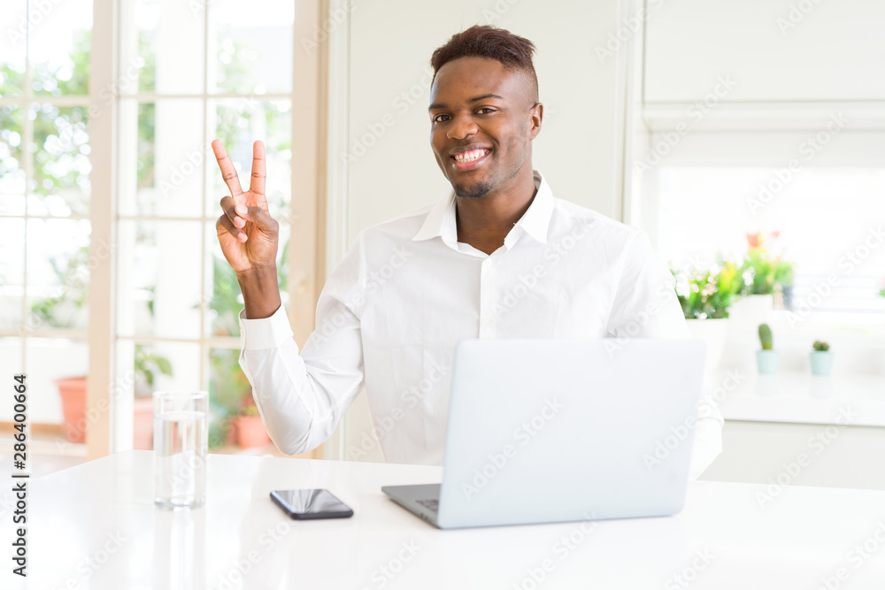 African american business man working using laptop smiling with happy face winking at the camera doing victory sign. Number two.
