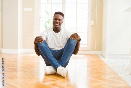 Handsome african american man sitting on the floor at home with a happy and cool smile on face. Lucky person.