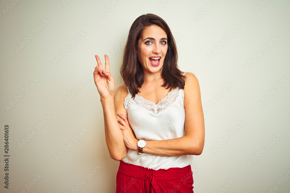 Young beautiful woman wearing t-shirt standing over white isolated background smiling with happy face winking at the camera doing victory sign. Number two. Young beautiful woman wearing t-shirt standing over white isolated background smiling with happy face winking at the camera doing victory sign. Number two.