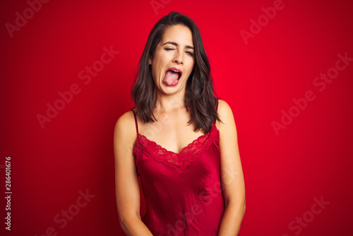 Young beautiful woman wearing sexy lingerie over red isolated background sticking tongue out happy with funny expression. Emotion concept.