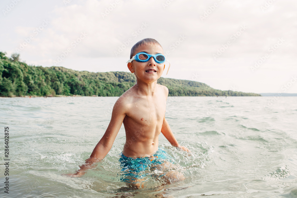 Cute funny Caucasian boy swimming in lake river with underwater goggles. Child diving in water on beach. Authentic real lifestyle happy childhood. Summer fun outdoor aquatic activity.