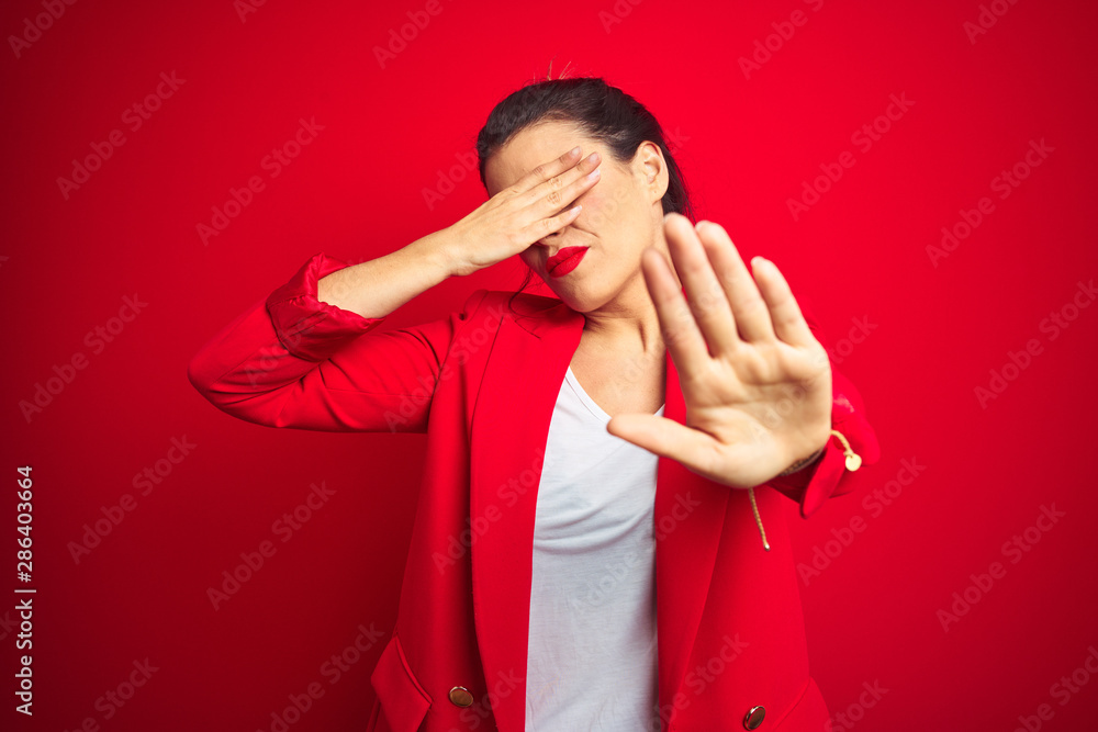 Young beautiful business woman standing over red isolated background covering eyes with hands and doing stop gesture with sad and fear expression. Embarrassed and negative concept.