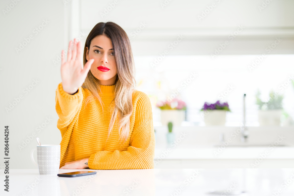 Young beautiful woman drinking a cup of coffee at home doing stop sing with palm of the hand. Warning expression with negative and serious gesture on the face. Young beautiful woman drinking a cup of coffee at home doing stop sing with palm of the hand. Warning expression with negative and serious gesture on the face.