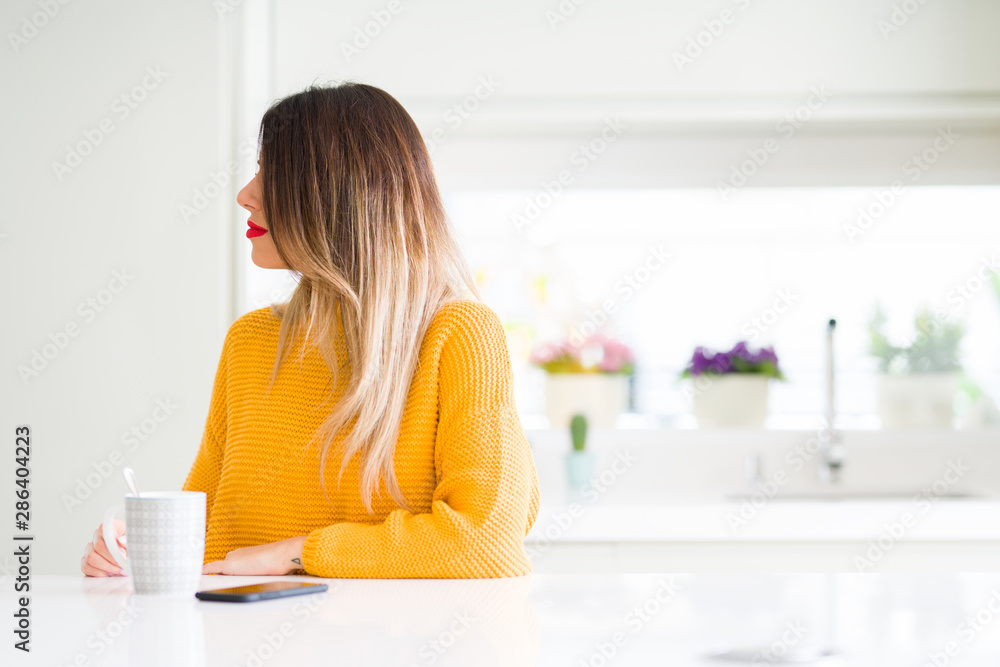 Young beautiful woman drinking a cup of coffee at home looking to side, relax profile pose with natural face with confident smile. Young beautiful woman drinking a cup of coffee at home looking to side, relax profile pose with natural face with confident smile.