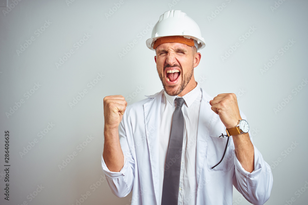 Young handsome engineer man wearing safety helmet over isolated background very happy and excited doing winner gesture with arms raised, smiling and screaming for success. Celebration concept. Young handsome engineer man wearing safety helmet over isolated background very happy and excited doing winner gesture with arms raised, smiling and screaming for success. Celebration concept.