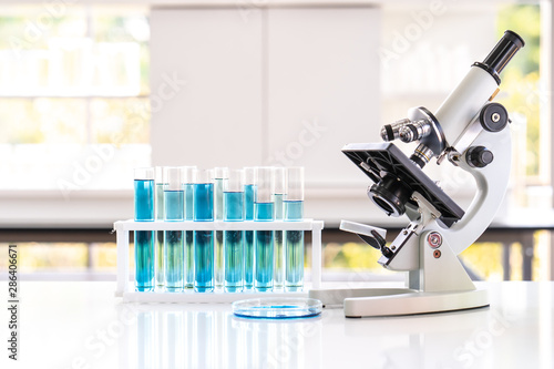 Closed up microscope with tube and glass in laboratory. Blue chemist in glass tubes on lab white table.
