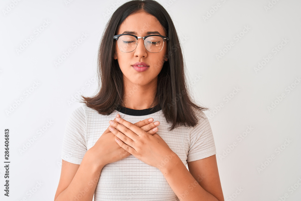Chinese woman wearing casual t-shirt and glasses standing over isolated white background smiling with hands on chest with closed eyes and grateful gesture on face. Health concept.