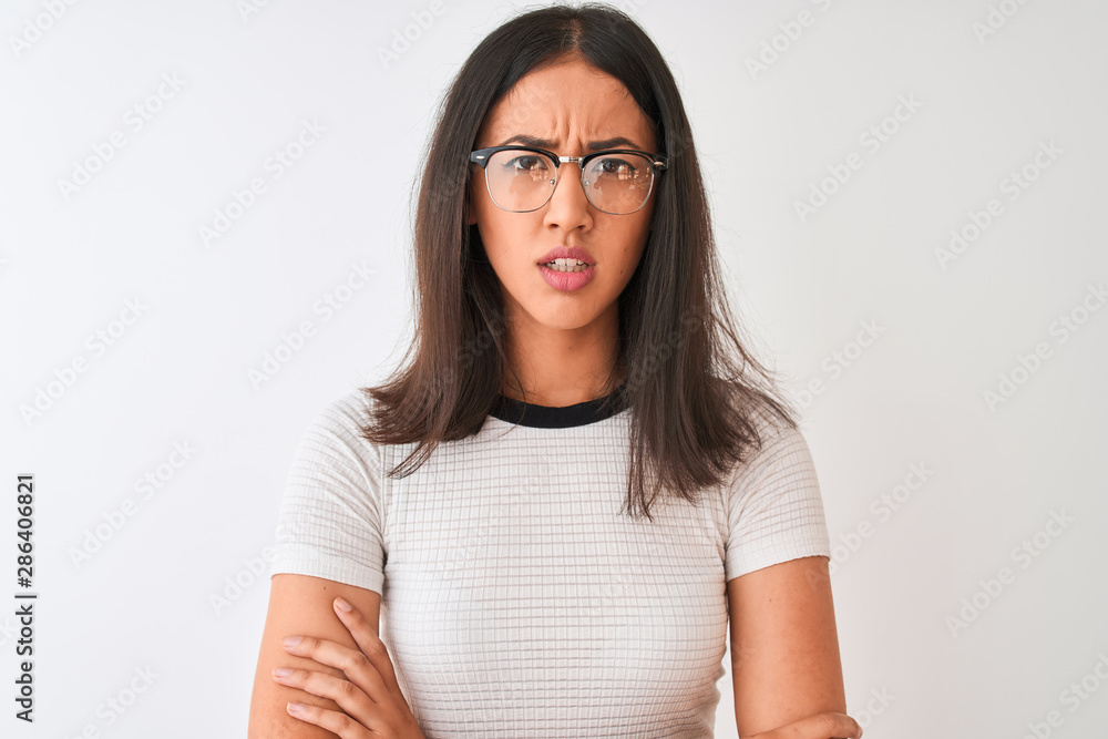 Chinese woman wearing casual t-shirt and glasses standing over isolated white background skeptic and nervous, disapproving expression on face with crossed arms. Negative person. Chinese woman wearing casual t-shirt and glasses standing over isolated white background skeptic and nervous, disapproving expression on face with crossed arms. Negative person.