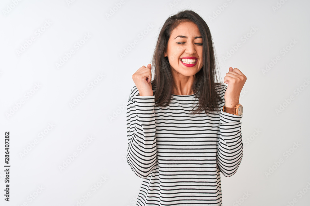 Young beautiful chinese woman wearing striped t-shirt standing over isolated white background excited for success with arms raised and eyes closed celebrating victory smiling. Winner concept. Young beautiful chinese woman wearing striped t-shirt standing over isolated white background excited for success with arms raised and eyes closed celebrating victory smiling. Winner concept.