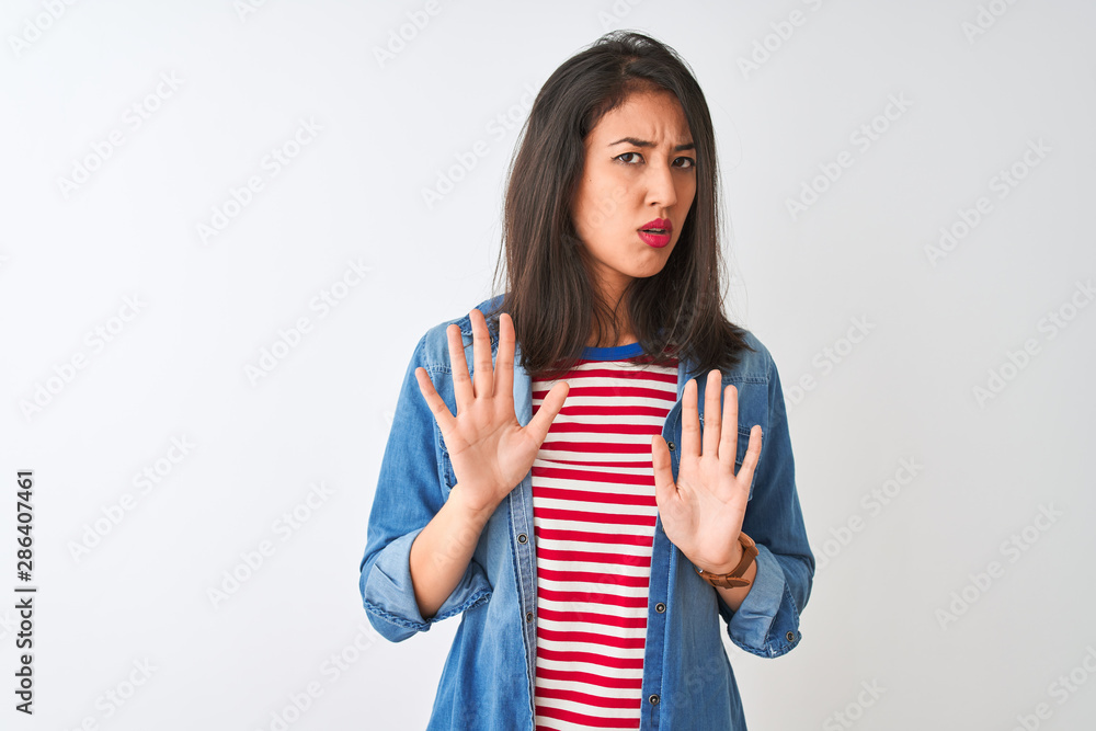 Young chinese woman wearing striped t-shirt and denim shirt over isolated white background Moving away hands palms showing refusal and denial with afraid and disgusting expression. Stop and forbidden. Young chinese woman wearing striped t-shirt and denim shirt over isolated white background Moving away hands palms showing refusal and denial with afraid and disgusting expression. Stop and forbidden.