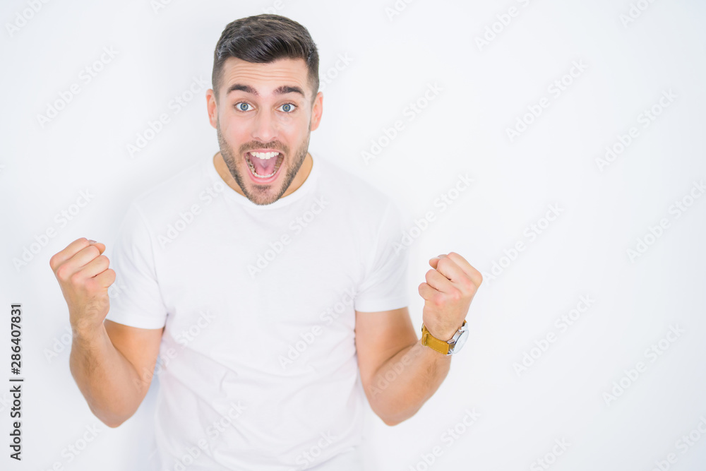 Young handsome man wearing casual white t-shirt over white isolated background celebrating surprised and amazed for success with arms raised and open eyes. Winner concept. Young handsome man wearing casual white t-shirt over white isolated background celebrating surprised and amazed for success with arms raised and open eyes. Winner concept.