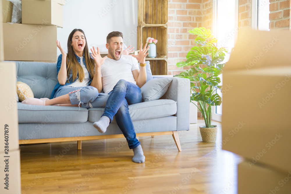 Young beautiful couple relaxing sitting on the sofa around boxes from moving to new house celebrating mad and crazy for success with arms raised and closed eyes screaming excited. Winner concept Young beautiful couple relaxing sitting on the sofa around boxes from moving to new house celebrating mad and crazy for success with arms raised and closed eyes screaming excited. Winner concept
