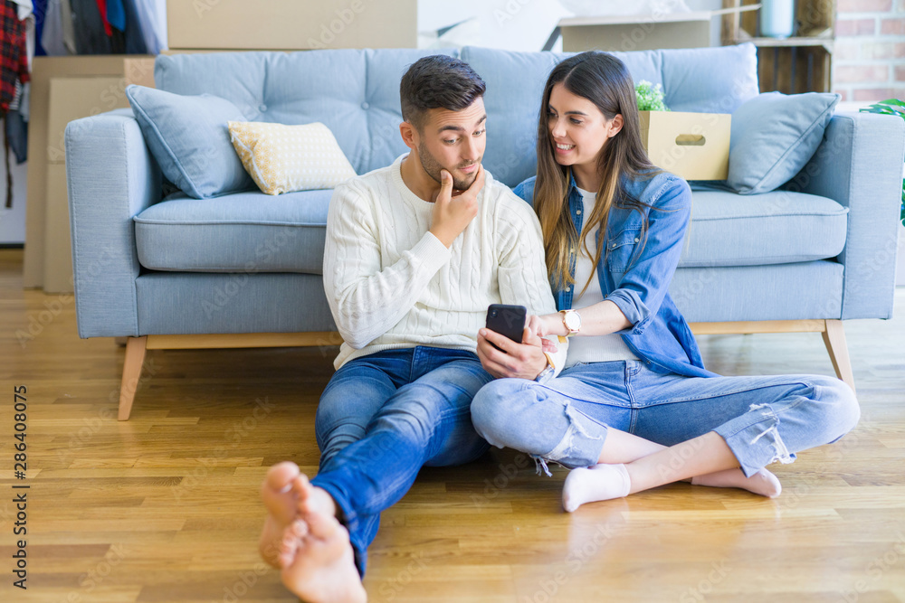 Young couple sitting on the floor of new home using smartphone and smiling happy for moving to a new home Young couple sitting on the floor of new home using smartphone and smiling happy for moving to a new home