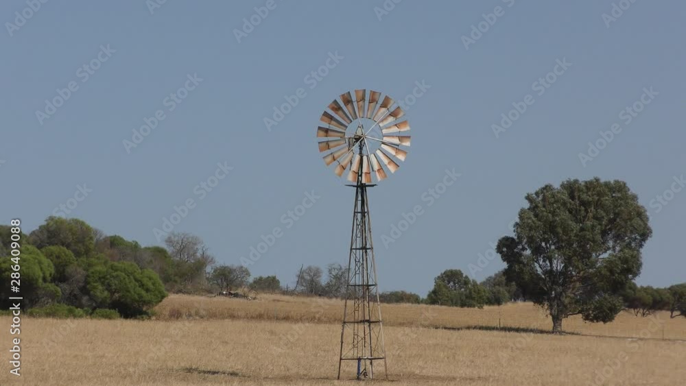 Iconic spinning wind mill on open field in outback Australia, with sunny blue sky and horizon as background. Iconic spinning wind mill on open field in outback Australia, with sunny blue sky and horizon as background.
