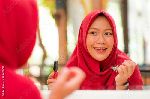 mirror reflection of young happy and beautiful Muslim woman in traditional hijab head scarf applying make up and cosmetics cheerful dolling up in beauty and fashion concept photo