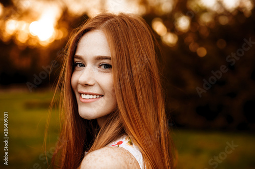 Canvas Print Close up portrait of a red hair woman girl with freckles looking at camera laughing over the shoulder against sunset outside