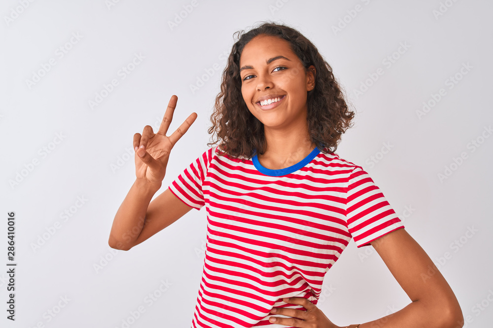 Young brazilian woman wearing red striped t-shirt standing over isolated white background smiling looking to the camera showing fingers doing victory sign. Number two. Young brazilian woman wearing red striped t-shirt standing over isolated white background smiling looking to the camera showing fingers doing victory sign. Number two.