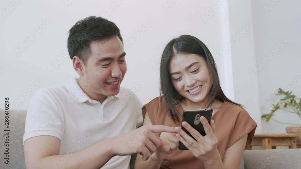 Asian Husband and wife sitting on the sofa and using touching smartphone they is smiling happy at home Asian Husband and wife sitting on the sofa and using touching smartphone they is smiling happy at home