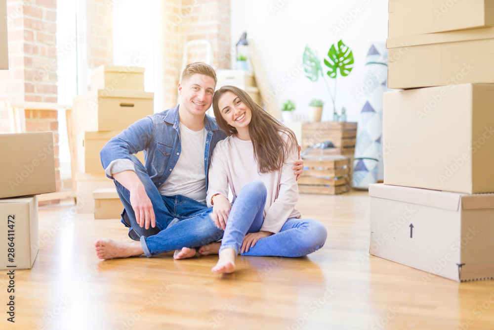 Young beautiful couple relaxing sitting on the floor around cardboard boxes at home, smiling happy moving to a new house