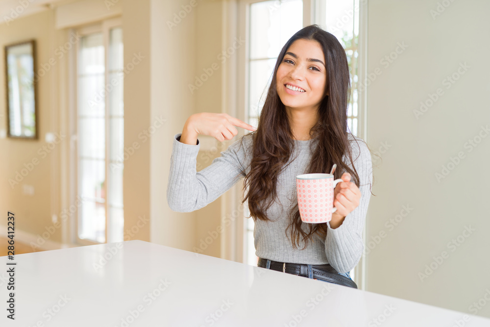 Young woman drinking a cup of coffee with surprise face pointing finger to himself