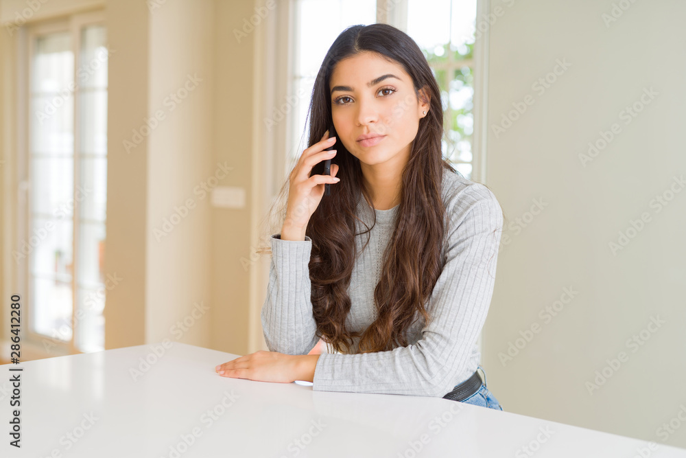 Young woman talking on the phone having a conversation with a confident expression on smart face thinking serious Young woman talking on the phone having a conversation with a confident expression on smart face thinking serious