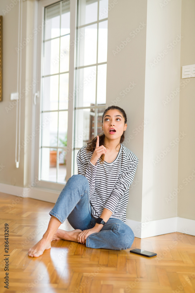 Beautiful young woman smiling cheerful pointing to the side with fingers sitting on the floor Beautiful young woman smiling cheerful pointing to the side with fingers sitting on the floor