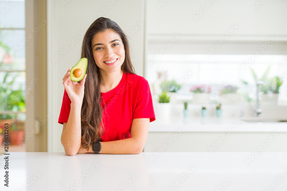 Young woman eating healthy avocado with a happy face standing and smiling with a confident smile showing teeth Young woman eating healthy avocado with a happy face standing and smiling with a confident smile showing teeth