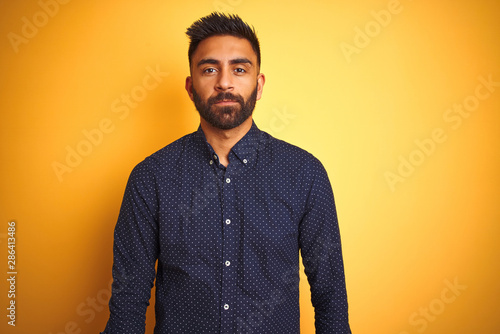 Young handsome indian businessman wearing shirt over isolated yellow background Relaxed with serious expression on face. Simple and natural looking at the camera.