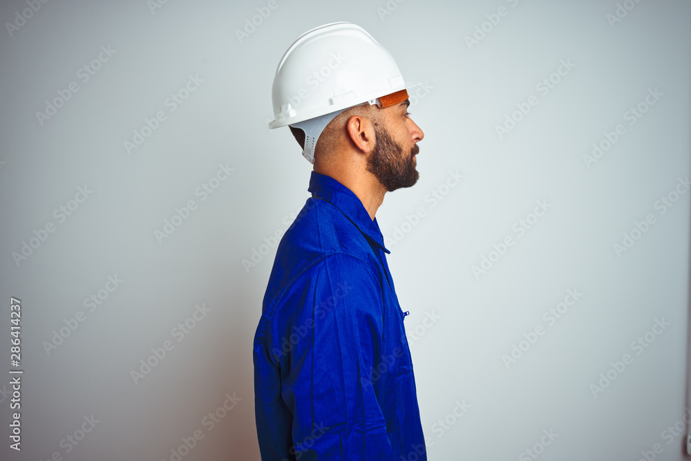 Handsome indian worker man wearing uniform and helmet over isolated white background looking to side, relax profile pose with natural face with confident smile.
